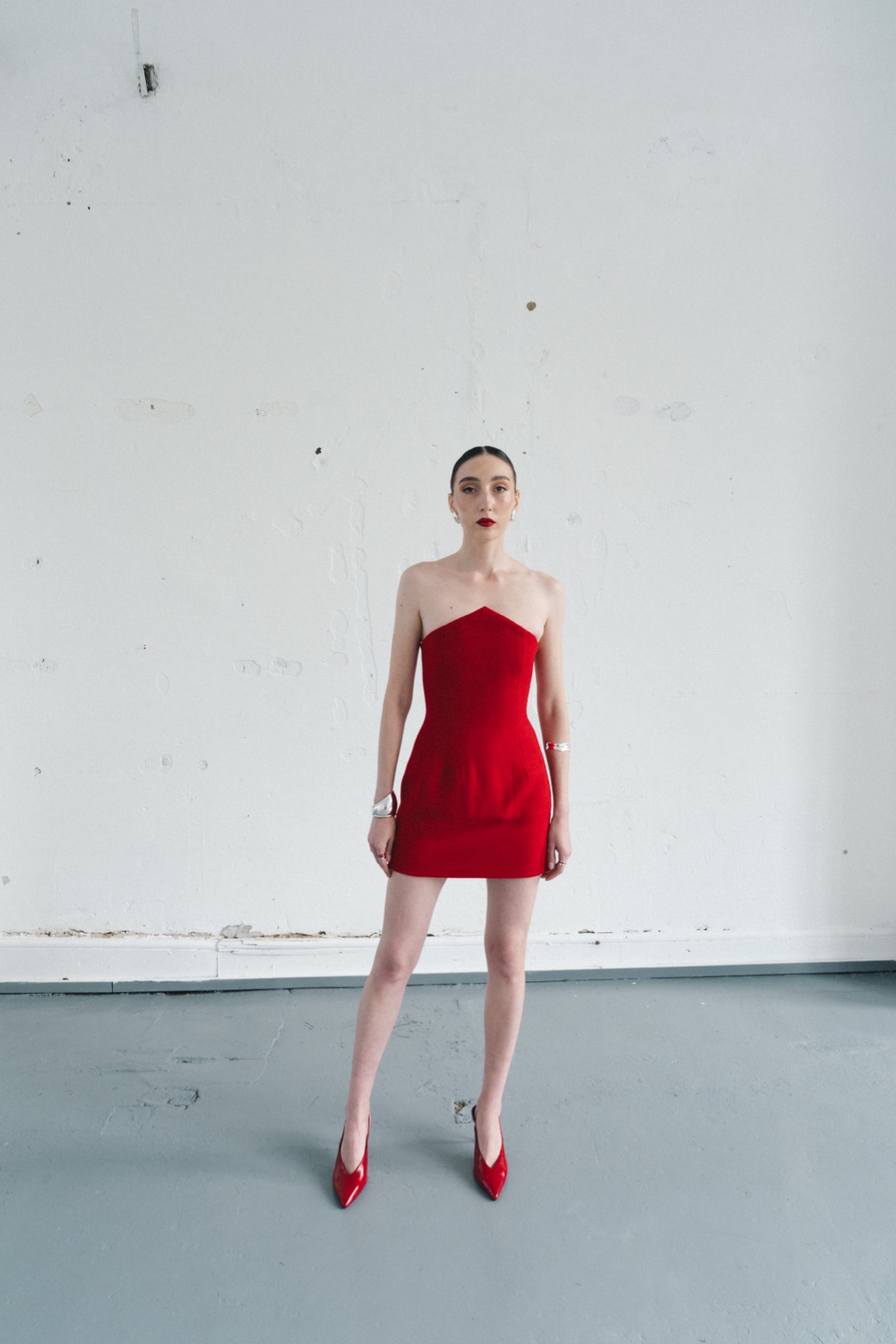 The red mini, full length from the front against a white plaster wall