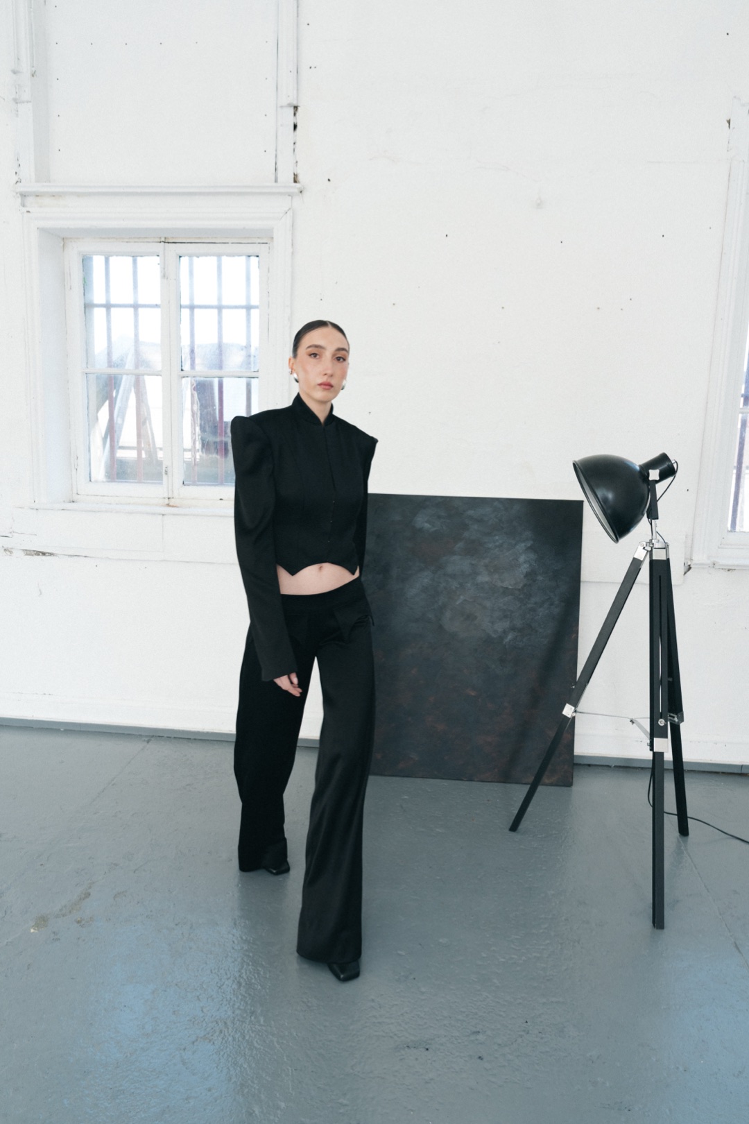 The black suit, full length, stepping forward beside a tripod studio lamp