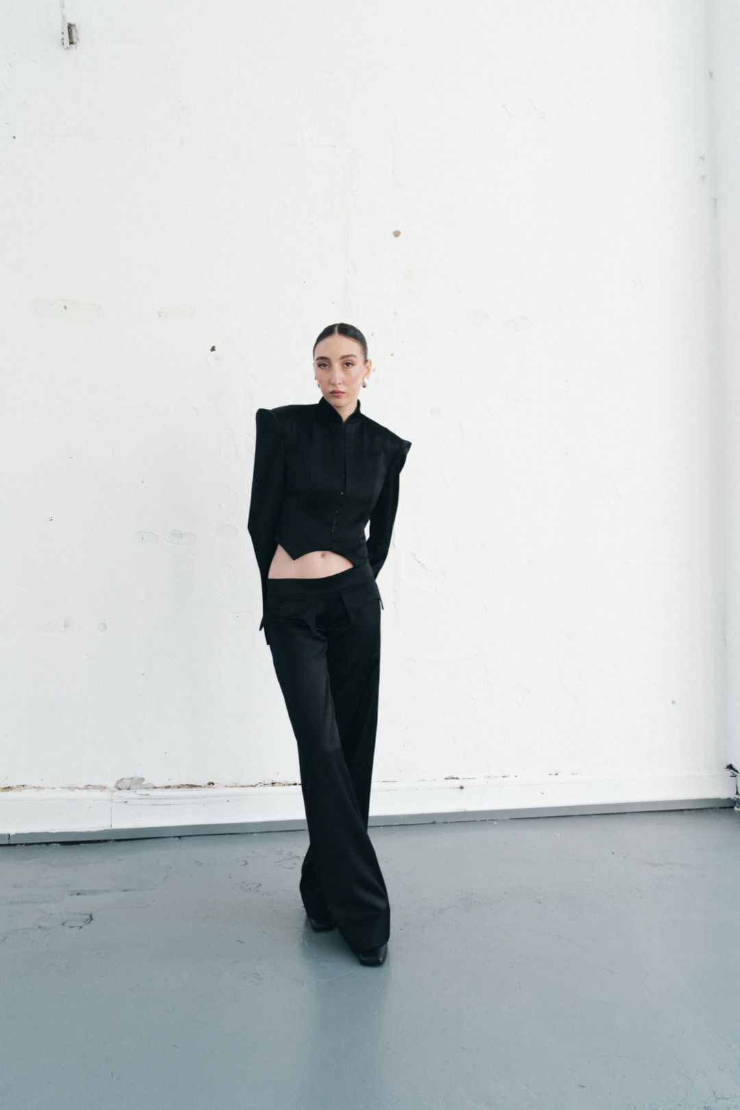 The black suit, front view, pointed hem and pockets against a white wall