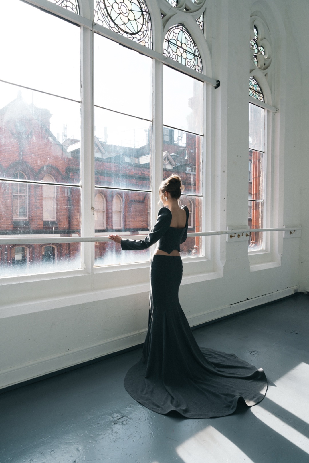 The grey bustier, back view at an arched window, the train across the floor