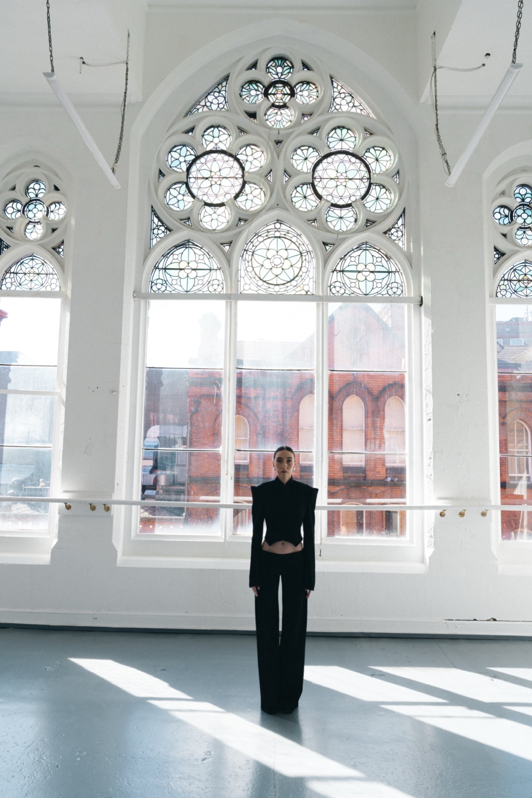 The black suit, standing beneath a tall Gothic tracery window in sunlight