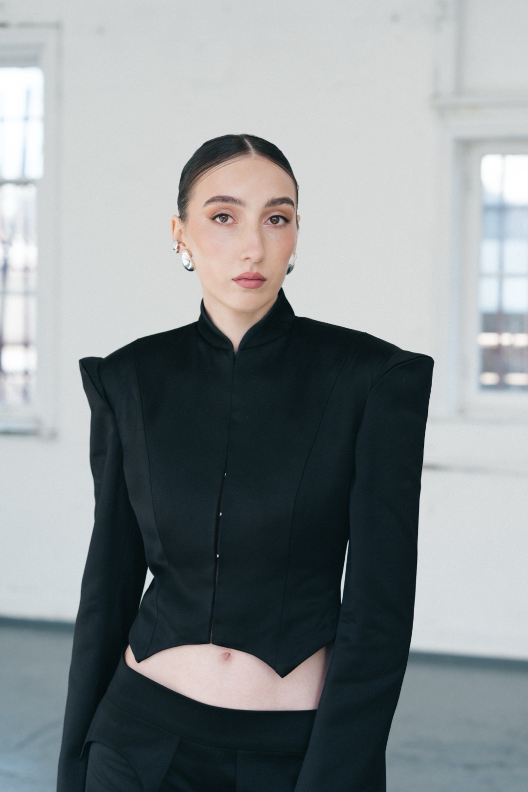 The black suit, half length, stand collar, sculptural shoulders and pointed hem