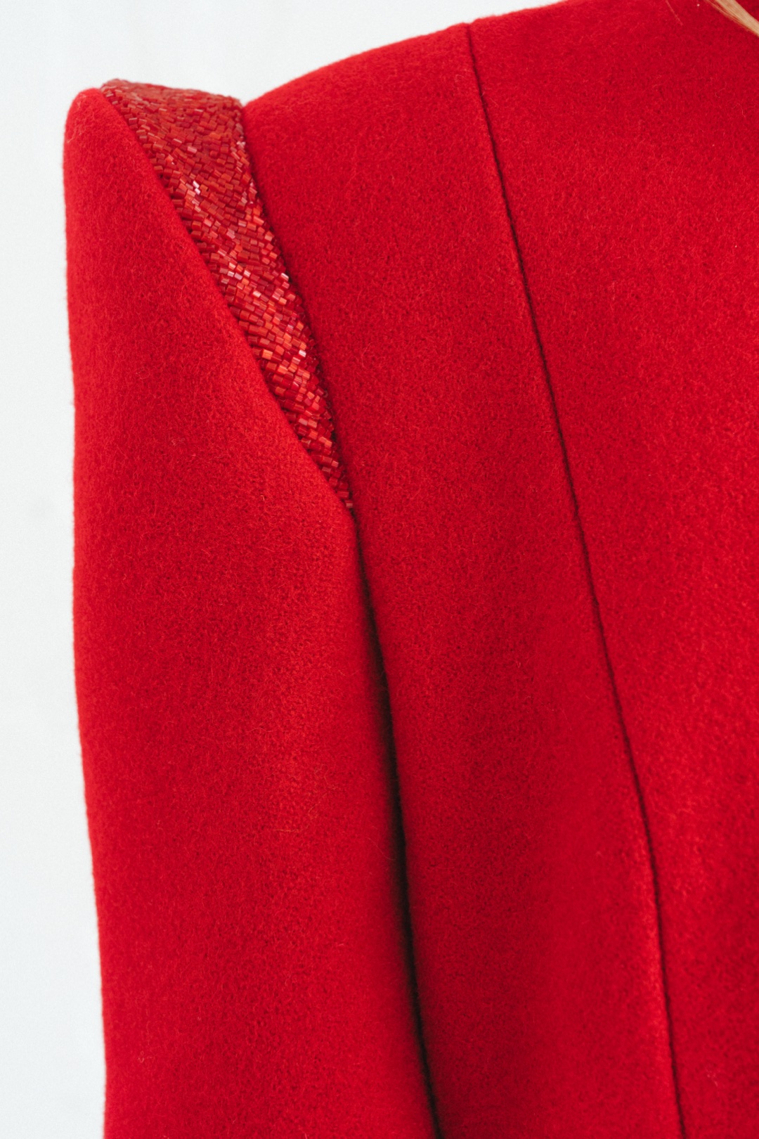 The red coat, close-up of beads tracing the line of the sculptural shoulder