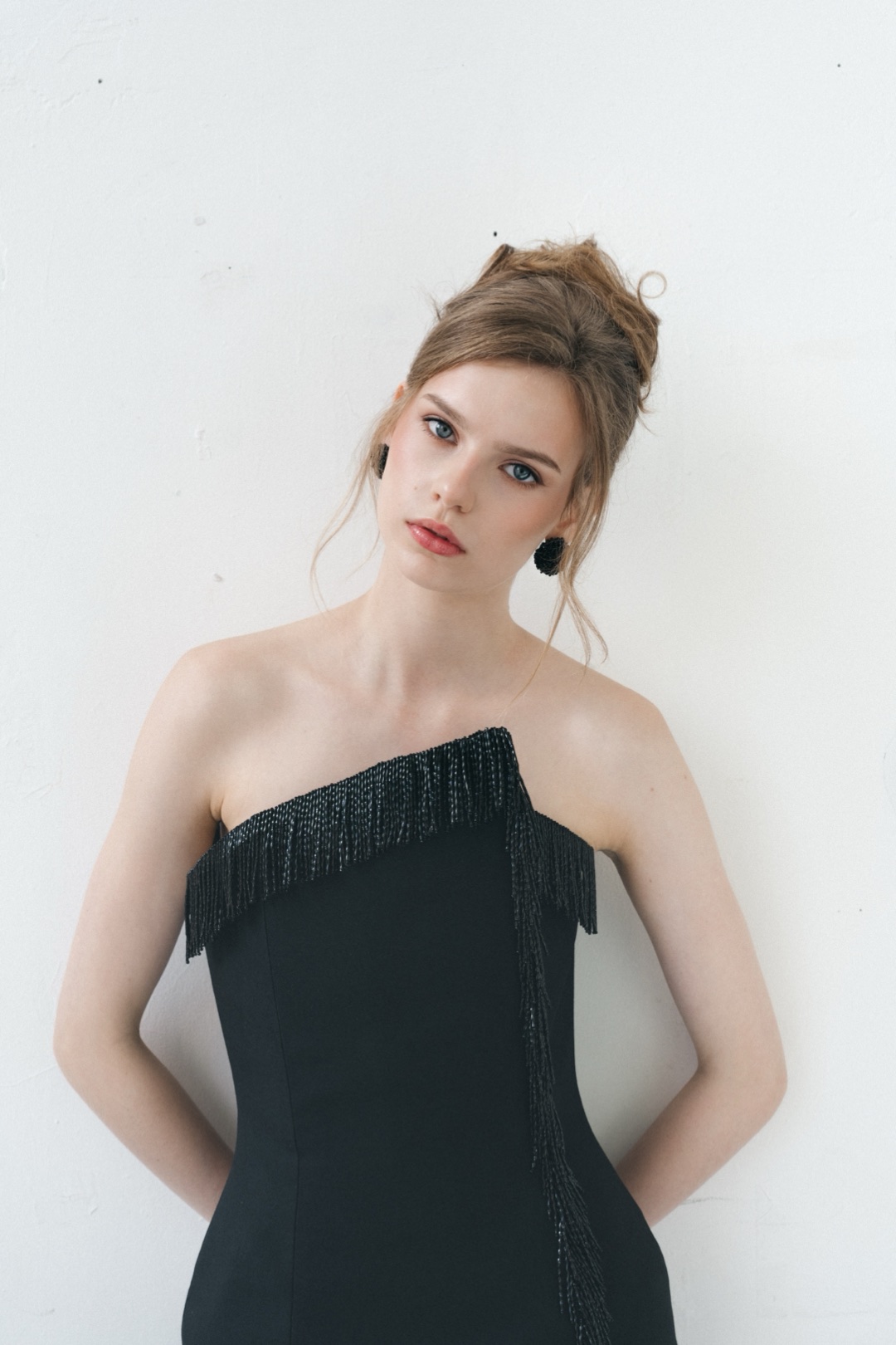 The fringe gown, the asymmetric neckline and bodice against a plain white wall