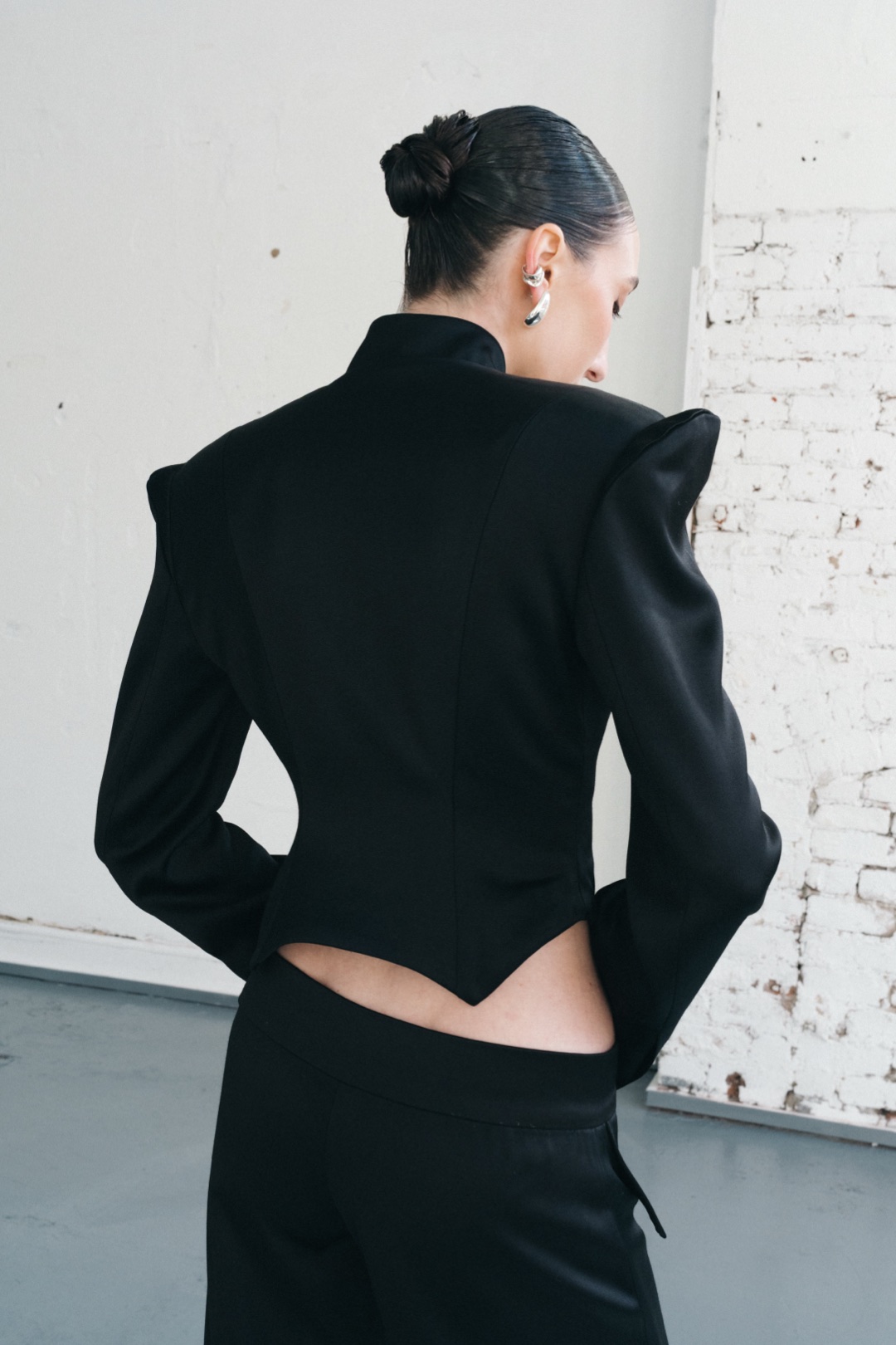 The black suit, back view of the sculptural shoulders and pointed hem