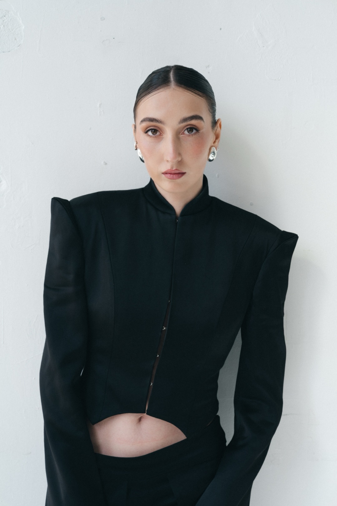The black suit, half length against a white wall, hook fastenings down the front