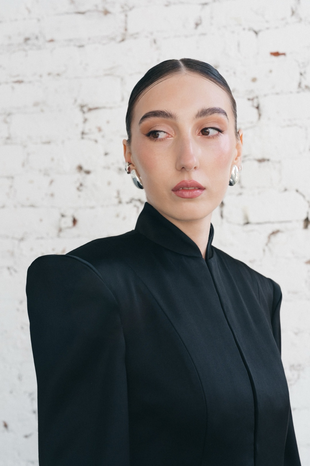 The black suit, close-up of the stand collar and shoulder against white brick