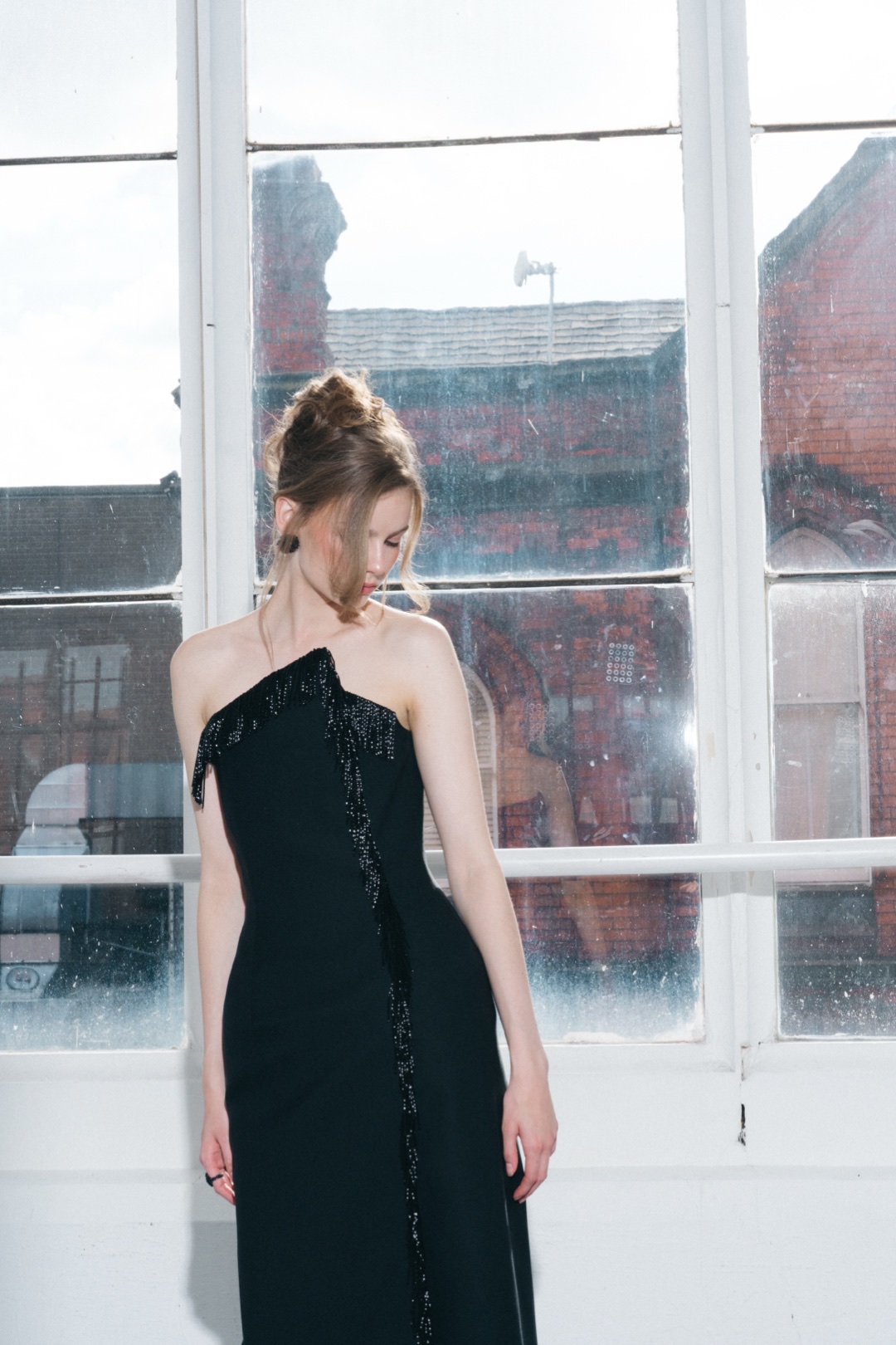 The fringe gown, head bowed before a sunlit window, fringe down the front