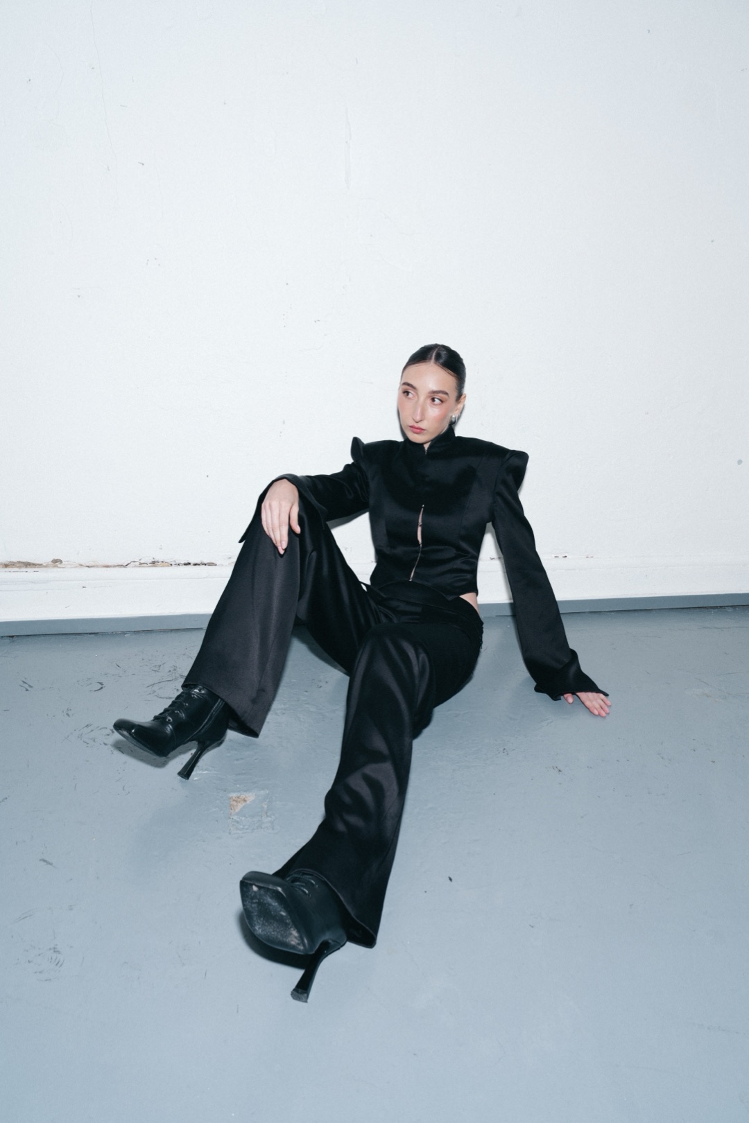 The black suit, seated on the studio floor, wide trousers stretched out