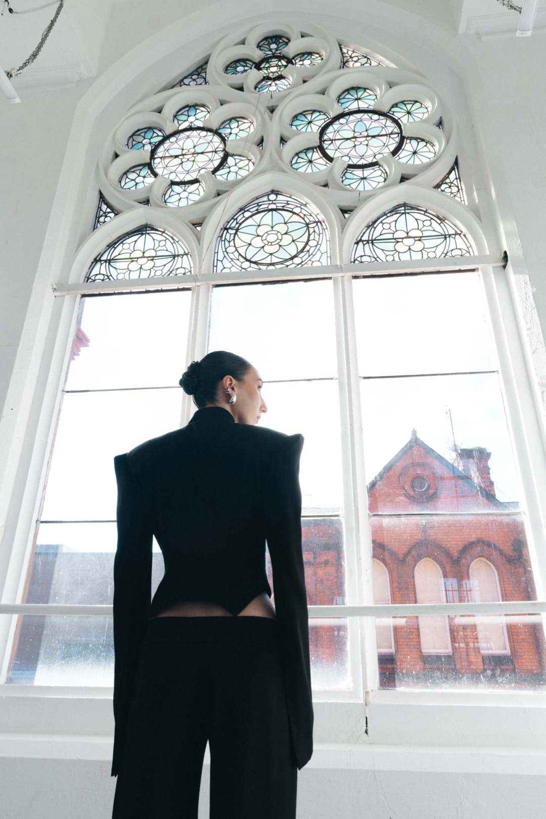 The black suit, back view beneath a Gothic tracery window, facing the street